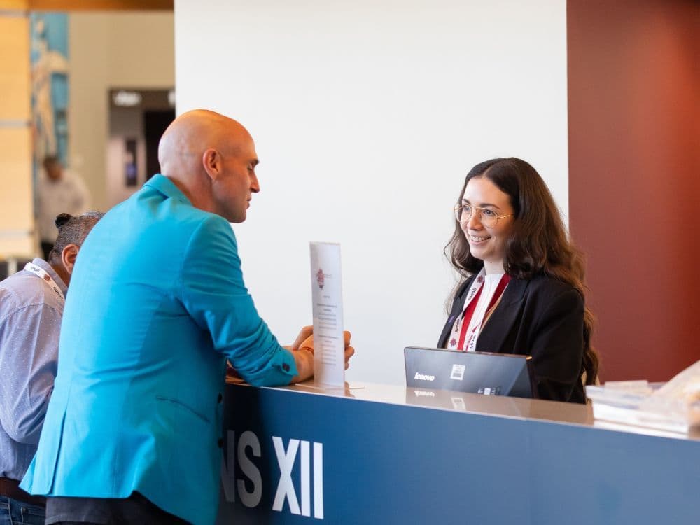 Conference attendee speaking with a ICMSA representative at an information desk.